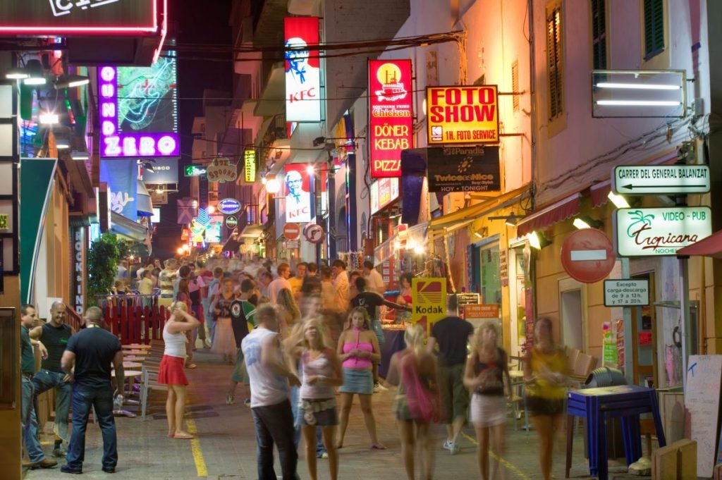 Imagem de uma rua comercial em Ibiza, na Espanha, à noite, cheia de pessoas na rua